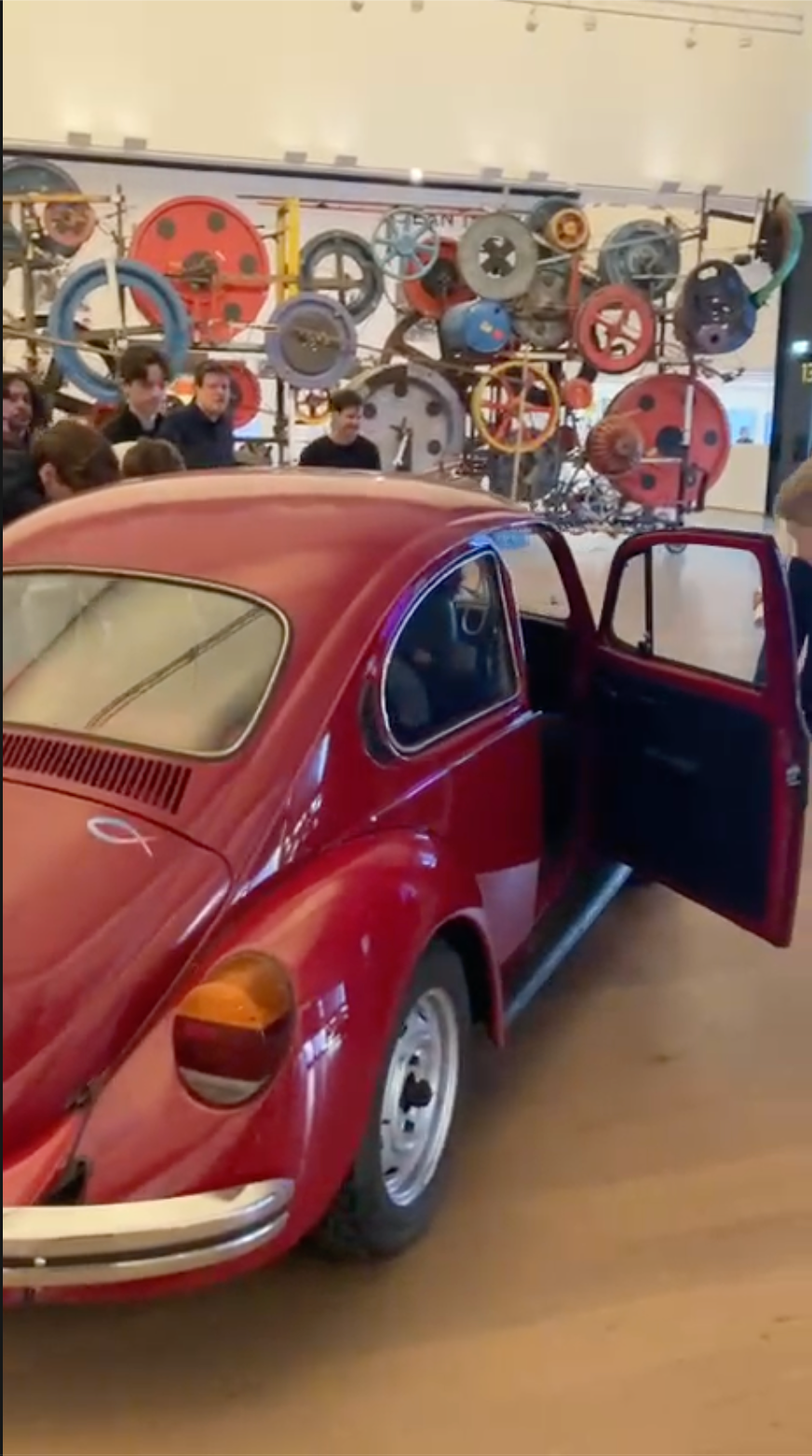 Roter VW Käfer mit geöffneter Tür vor einer Tinguely-Installation